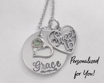 May include: Silver necklace with a round pendant that says "Grace" with an arrow and a heart. The pendant also has a small green gemstone. The necklace also has a heart-shaped charm that says "Sweet 16". The text "Personalized for You!" is written below the necklace.