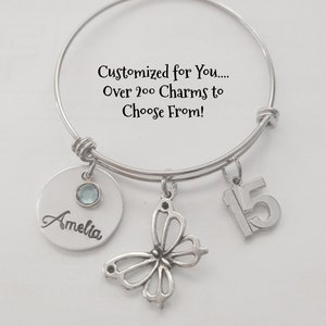 May include: A silver charm bracelet with a butterfly charm, a charm with the number 15, and a personalized charm with the name Amelia. The bracelet has a message that says "Customized for You... Over 200 Charms to Choose From!"
