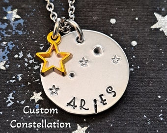 May include: Silver necklace with a round pendant featuring the Aries constellation and the word "Aries" written on it. A small gold star charm hangs from the pendant.