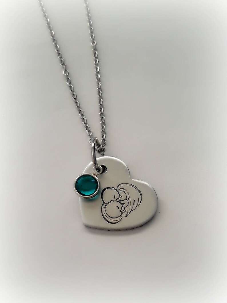 May include: A silver heart-shaped pendant necklace with a small teal gemstone and an engraved image of two babies.