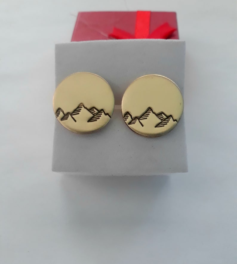 Puede incluir: Un par de pendientes de color dorado con un dise&ntilde;o de cordillera. Los pendientes son redondos y tienen un acabado liso y pulido.
