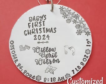 以下が含まれることがあります： 「BABY'S FIRST CHRISTMAS 2024」と「Willow April Wilson」の文字が刻まれた銀色の丸いオーナメント。2024年10月24日午前8時18分生まれ、体重3.2kg。雪の結晶とヒイラギの葉で飾られています。