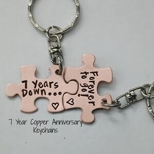 May include: Two copper-colored puzzle piece keychains with the text "7 Years Down..." and "Forever to go!" engraved on them. The keychains are connected by a silver ring.