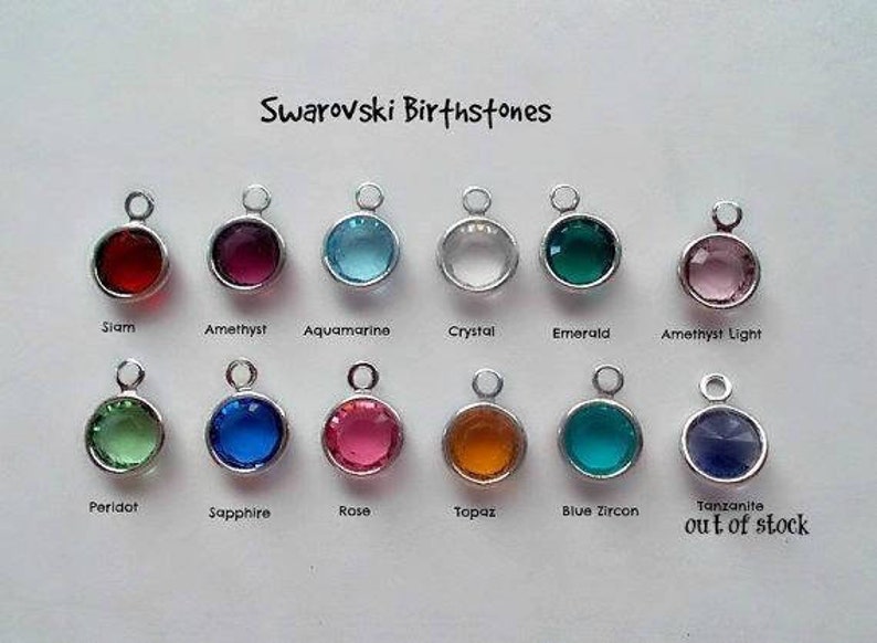 May include: A chart of Swarovski birthstones, showing a variety of colors and styles. The birthstones are arranged in two rows, with the names of each stone listed below. The chart includes the following birthstones: Siam, Amethyst, Aquamarine, Crystal, Emerald, Amethyst Light, Peridot, Sapphire, Rose, Topaz, Blue Zircon, and Tanzanite.