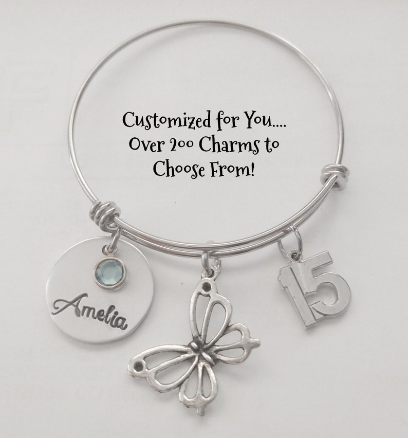 May include: A silver charm bracelet with a butterfly charm, a charm with the number 15, and a personalized charm with the name Amelia. The bracelet has a message that says "Customized for You... Over 200 Charms to Choose From!"