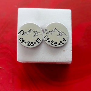 Puede incluir: Dos pendientes de plata con un dise&ntilde;o de cordillera y la fecha "09.28.19" grabada en cada uno.
