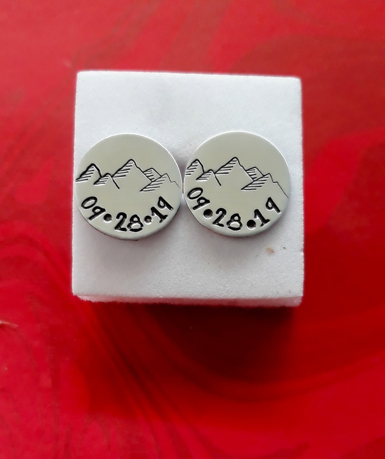 Puede incluir: Dos pendientes de plata con un dise&ntilde;o de cordillera y la fecha "09.28.19" grabada en cada uno.