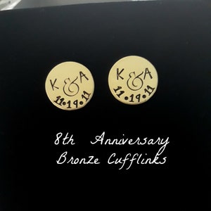 May include: A pair of gold-toned cufflinks with the initials "K & A" and the date "11.19.11" engraved on each. The cufflinks are labeled "8th Anniversary Bronze Cufflinks".