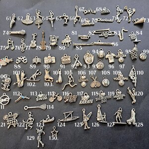 May include: A collection of 130 silver charms featuring various sports, activities, and hobbies. The charms are arranged in rows on a white background. Some of the charms include a basketball, a soccer ball, a baseball, a tennis racket, a volleyball, a skateboard, a bicycle, a running shoe, a karate belt, a microphone, a musical note, a violin, a piano, a paintbrush, a pair of glasses, a camera, a typewriter, a baseball glove, a soccer jersey, a basketball hoop, a ski, a snowboard, a baseball bat, a tennis ball, a volleyball, a cross, a lacrosse stick, a canoe, a surfboard, a skateboard, a roller skate, and a star.