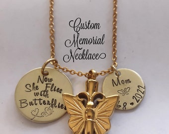 Op de afbeelding: Gouden ketting met een vlinderhanger en twee ronde bedels. De bedels hebben de tekst "Now She Flies with Butterflies" en "Mom 8.2022".