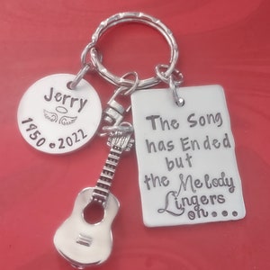 May include: Silver keychain with a guitar charm, a round tag that says "Jerry 1950-2022" with an angel wing design, and a rectangular tag that says "The song has ended but the melody lingers on..."