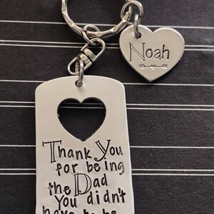 May include: Silver keychain with a heart-shaped tag that says "Thank You for being the Dad You didn't have to be" and a smaller heart-shaped tag with the name "Noah" engraved on it.
