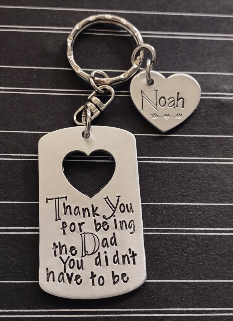 May include: Silver keychain with a heart-shaped tag that says "Thank You for being the Dad You didn't have to be" and a smaller heart-shaped tag with the name "Noah" engraved on it.