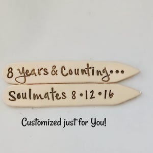 Puede incluir: Dos etiquetas de madera grabadas con el texto "8 años y contando..." y "Soulmates 8.12.16".