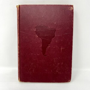 May include: A burgundy hardback book with a silhouette of South America on the front cover.