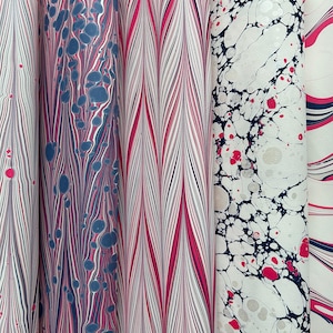 May include: A selection of patterned paper rolls, featuring various designs. The patterns include stripes, chevrons, and marbled effects in white, pink, blue, and black. The paper is suitable for crafts, scrapbooking, or gift wrapping, with measurements in centimetres.