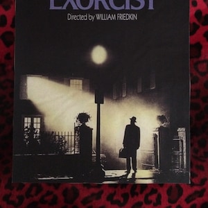 Pode incluir: Um cartaz de filme para o filme "O Exorcista" dirigido por William Friedkin. O cartaz apresenta uma cena de rua escura e sombria com um homem que se afasta da câmera, carregando uma maleta. O título do filme está em letras grandes de cor púrpura.