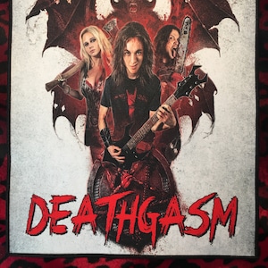 Może przedstawiać: Prostokątna naszywka z czerwoną i czarną obwódką, przedstawiająca grupę osób z demonicznym tłem. Słowo "DEATHGASM" jest napisane na czerwono, kapującymi literami.
