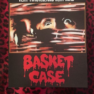 May include: A vintage movie poster for the horror film "Basket Case". The poster features a close-up of a person's face peering through a wicker basket, with the text "THE TENANT IN ROOM 7 IS VERY SMALL, VERY TWISTED, AND VERY MAD" at the top and "BASKET CASE" in red dripping letters at the bottom.