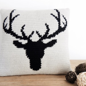 May include: A white crocheted pillow with a black silhouette of a deer head with antlers.