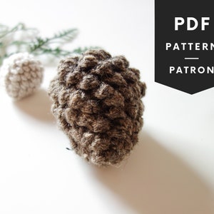May include: A brown crocheted pinecone ornament with a smaller white crocheted pinecone ornament in the background. The image includes the text "PDF PATTERN PATRON".