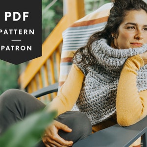 May include: A woman wearing a grey crocheted cowl neck sweater and a yellow long-sleeved shirt. The sweater has a textured stitch pattern. The woman is sitting in a chair on a porch.