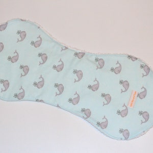 May include: A light blue burp cloth with a white border and a pattern of grey whales with a small green sprig. The cloth has a small orange label that says "Little Sprout".