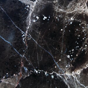 May include: Black marble with white veins and speckles. The marble has a dark, almost black, background with a network of white veins and small white speckles throughout.