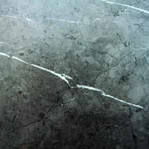 May include: A close-up of a grey marble surface with white veins. The surface has a rough texture and a slightly faded appearance.