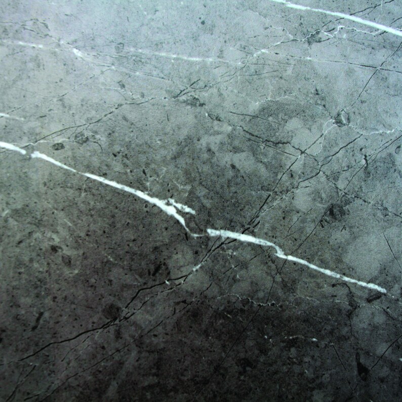 May include: A close-up of a grey marble surface with white veins. The surface has a rough texture and a slightly faded appearance.