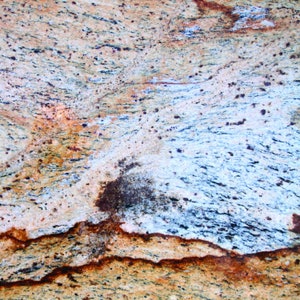 Puede incluir: Primer plano de una encimera de granito colorida con un patr&oacute;n de remolino de marr&oacute;n, amarillo, azul y blanco. La superficie tiene una textura rugosa.