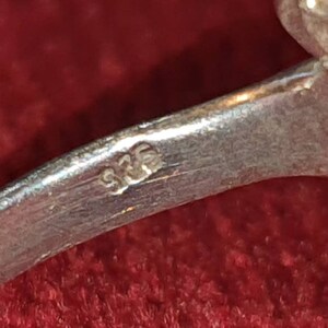 May include: Close-up of a silver ring with the number "925" stamped on the inside band.