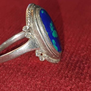 May include: A silver ring with a blue and green oval gemstone set in a bezel setting. The ring has a decorative band with a beaded edge.