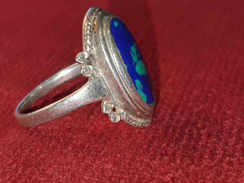 May include: A silver ring with a blue and green oval gemstone set in a bezel setting. The ring has a decorative band with a beaded edge.