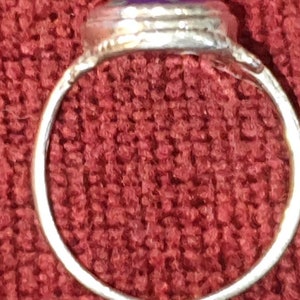 May include: A silver ring with a purple stone set in the center. The ring is on a red fabric background.