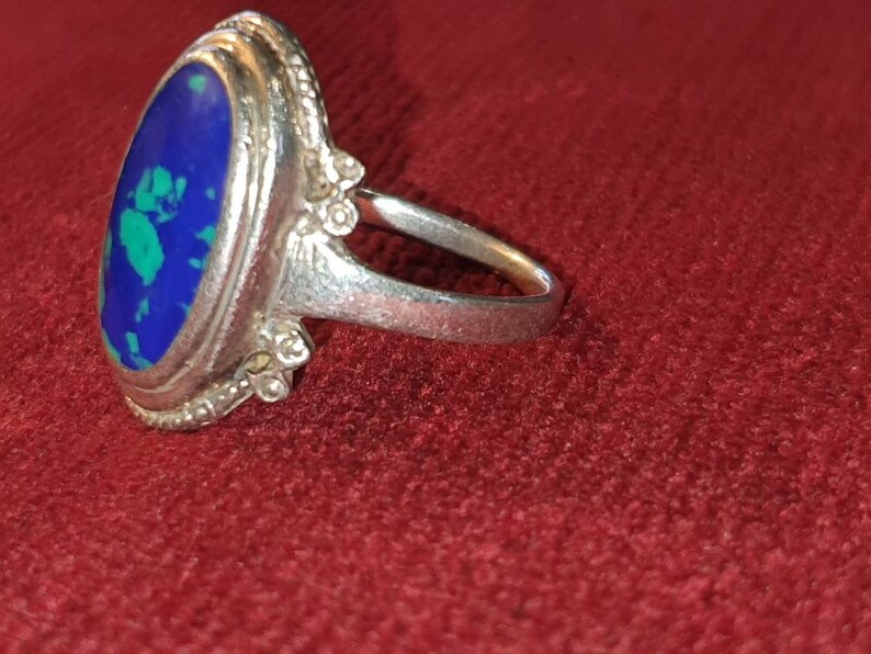 May include: A silver ring with an oval-shaped blue and green gemstone set in a decorative silver bezel.