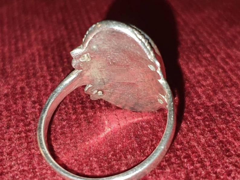 May include: Silver ring with a detailed design on the band and a large oval-shaped stone setting.
