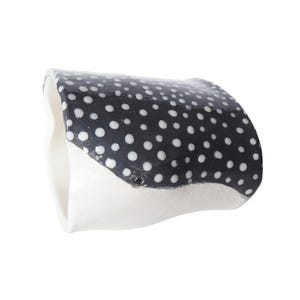 May include: A ceramic ring dish shaped like a manta ray. The dish features a black and white polka dot pattern on the top surface and a white underside. A small, dark detail represents an eye.