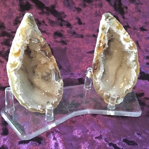 May include: Two agate geode halves with clear quartz crystals inside, displayed on a clear acrylic stand.