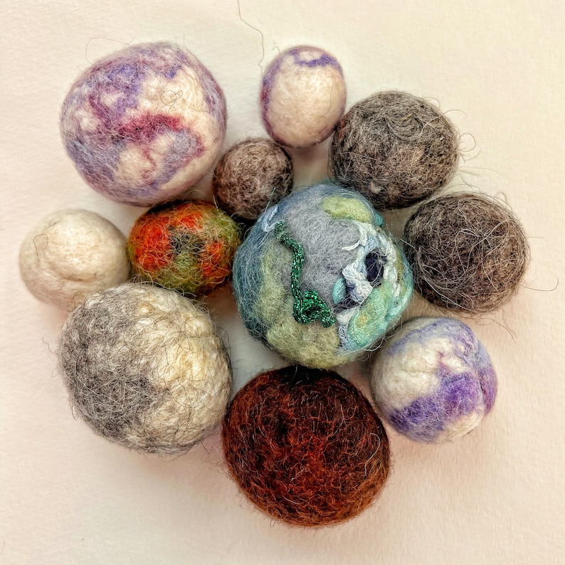 Pu&ograve; includere: Una collezione di dieci palline di lana feltrata in vari colori e motivi, tra cui viola, blu, verde, marrone e bianco. Le palline sono tutte pi&ugrave; o meno della stessa dimensione e sono disposte in un cerchio.