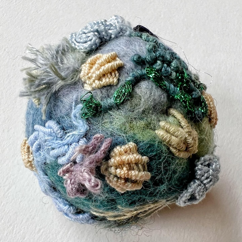 Pu&ograve; includere: Una piccola scultura rotonda in feltro con una variet&agrave; di texture e colori. La scultura &egrave; realizzata in lana e presenta una variet&agrave; di colori, tra cui blu, verde e beige. La scultura &egrave; decorata con una variet&agrave; di texture, tra cui lisce, ruvide e irregolari.