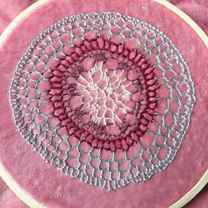 May include: A close-up of a pink velvet fabric with a silver and red crocheted doily in the center.
