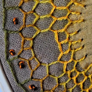 May include: Close-up of a gray fabric with a yellow, orange, and green embroidered design. The design is a series of connected hexagons.