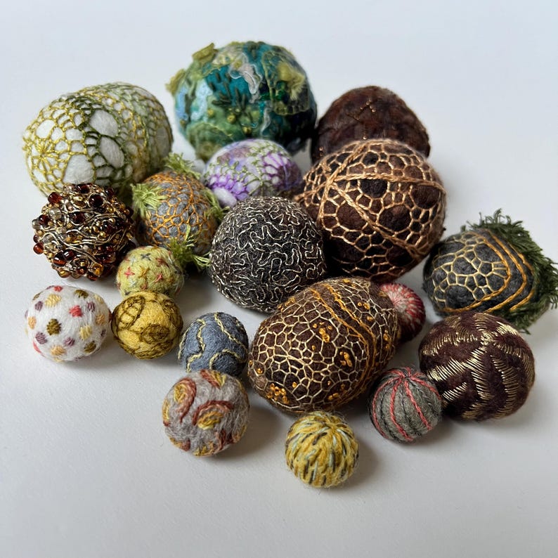 Pu&ograve; includere: Una collezione di piccole sfere cucite a mano in vari colori e trame, tra cui marrone, oro, verde, bianco e grigio. Le sfere sono decorate con ricami e perline intricate.