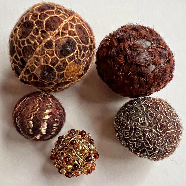 Pu&ograve; includere: Cinque ornamenti in feltro marrone e oro con disegni intricati. Gli ornamenti sono rotondi e hanno una variet&agrave; di texture, tra cui un motivo intrecciato, una texture pelosa e una texture liscia. Gli ornamenti sono decorati con filo d'oro e perline.