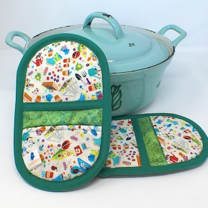 Könnte beinhalten: Ein hellblaues Emaille-Kochtopf mit Deckel und zwei grünen Ofenhandschuhen. Die Handschuhe haben einen weißen Hintergrund mit bunten Gartenmustern und grünen Zierleisten. Die Handschuhe sollen die Hände vor Hitze schützen.