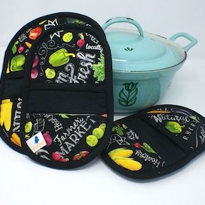 May include: Three black pot holders with a colorful vegetable and chalkboard design. The pot holders have a pocket on the back. The text on the pot holders reads "Farmer's Market", "Fresh", "Healthy", and "Natural".