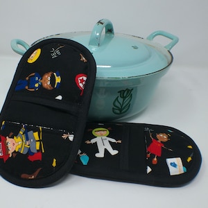 Könnte beinhalten: Zwei schwarze Topflappen mit einem farbenfrohen Cartoon-Aufdruck von Kindern in verschiedenen Berufen, darunter ein Feuerwehrmann, ein Astronaut und ein Polizist. Im Hintergrund ein hellblauer Emailletopf.