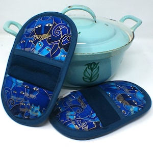 May include: Two blue and gold cat print pot holders with a blue background. The pot holders are oval shaped and have a dark blue border.