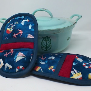 Könnte beinhalten: Zwei blaue und rote Topflappen mit nautischem Thema. Die Topflappen haben einen blauen Hintergrund mit weißen Segelbooten, roten Ankern und roten und weißen Rettungsringen. Die Topflappen haben einen roten Stoffeinsatz.